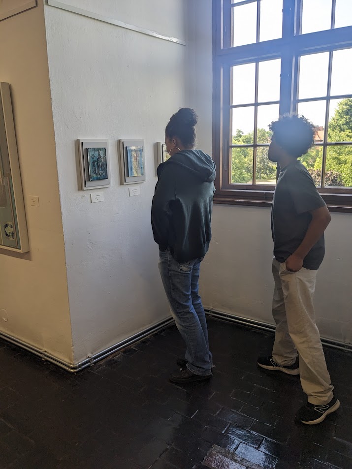 Zwei junge Menschen stehen vor drei kleinen Bildern von Carola Helbing-Erbenn